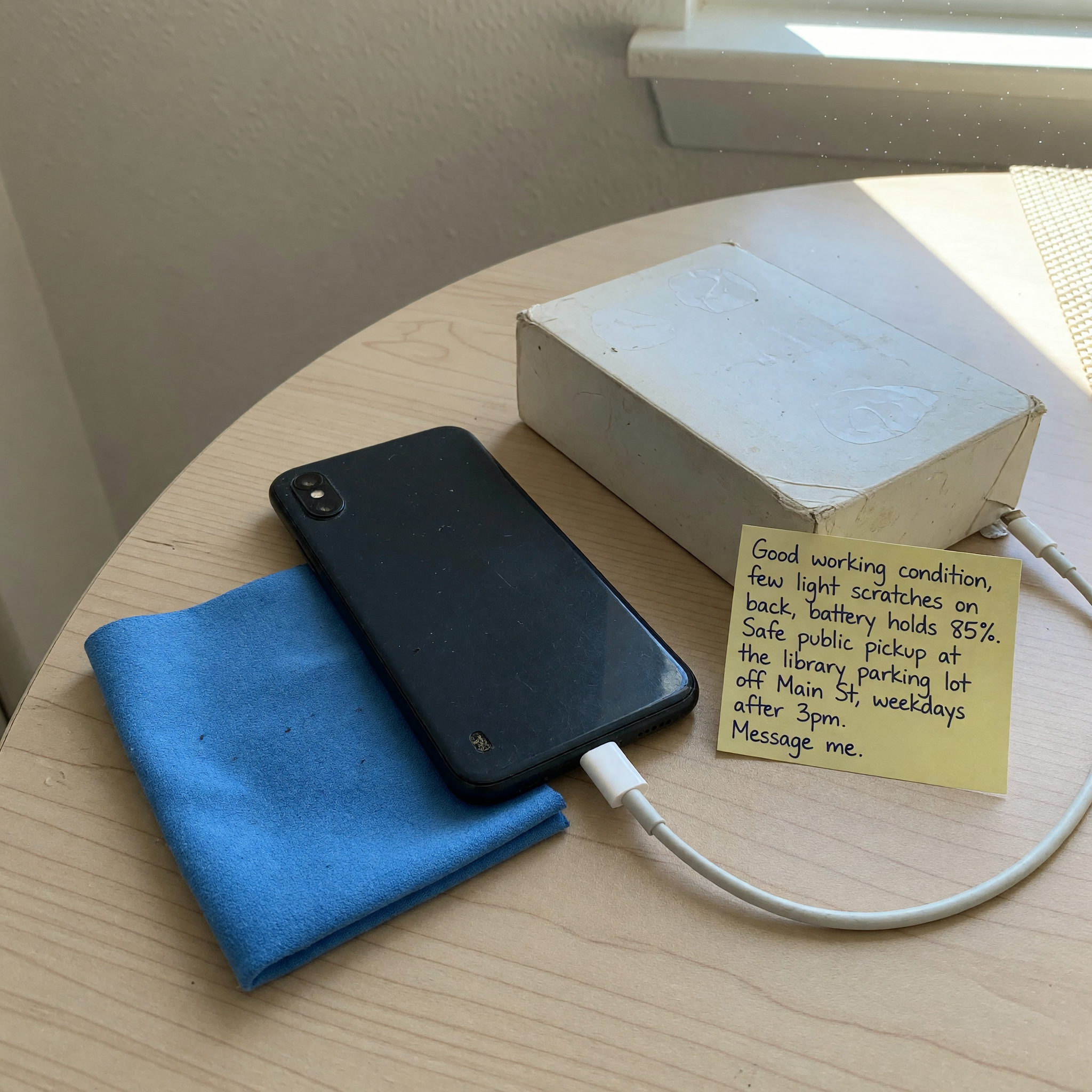Celular usado sobre una mesa con cargador, caja, nota de IMEI, paño de limpieza y fotos de estado listas para un anuncio