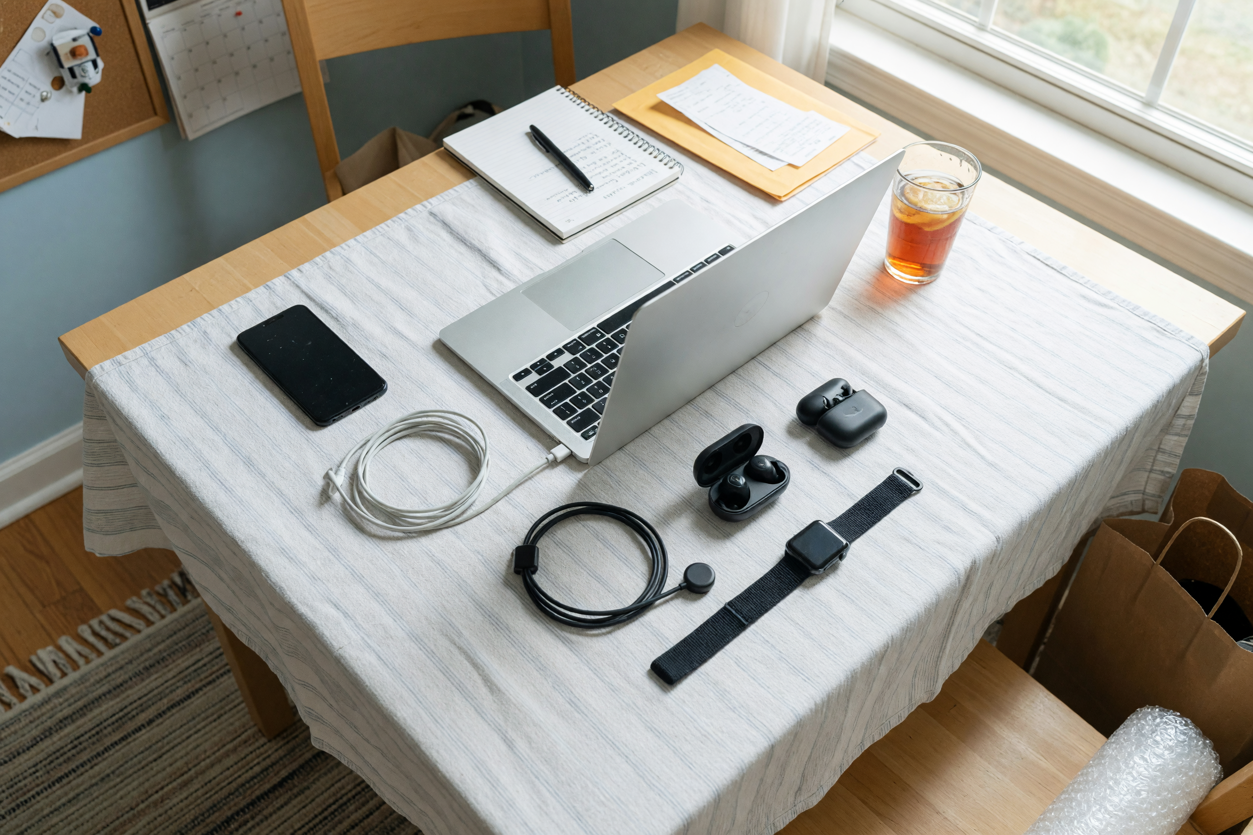 A phone, open laptop, earbuds, smartwatch, and charging cables laid out on a table to photograph for a local electronics listing
