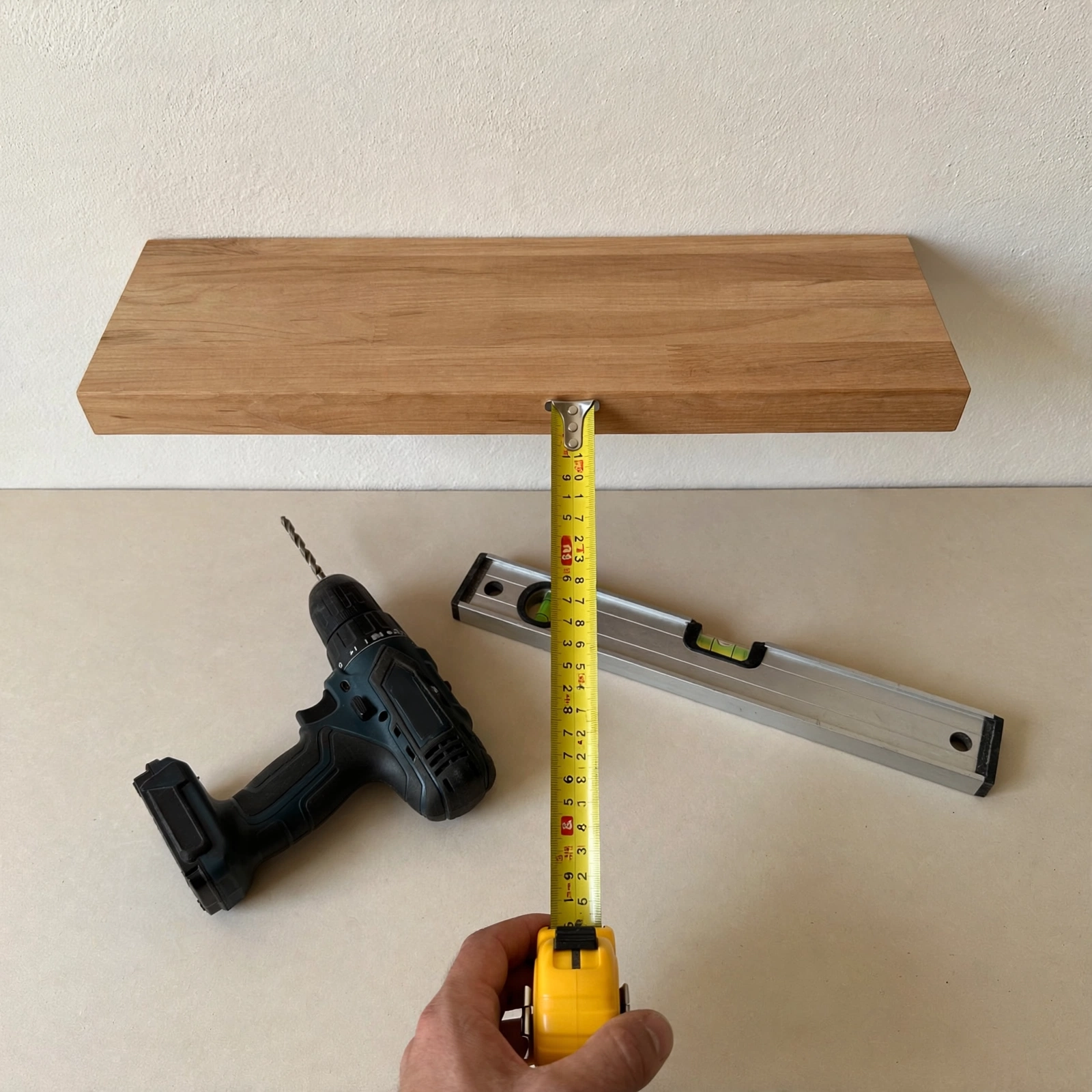 A drill, level, and tape measure beside a finished shelf install