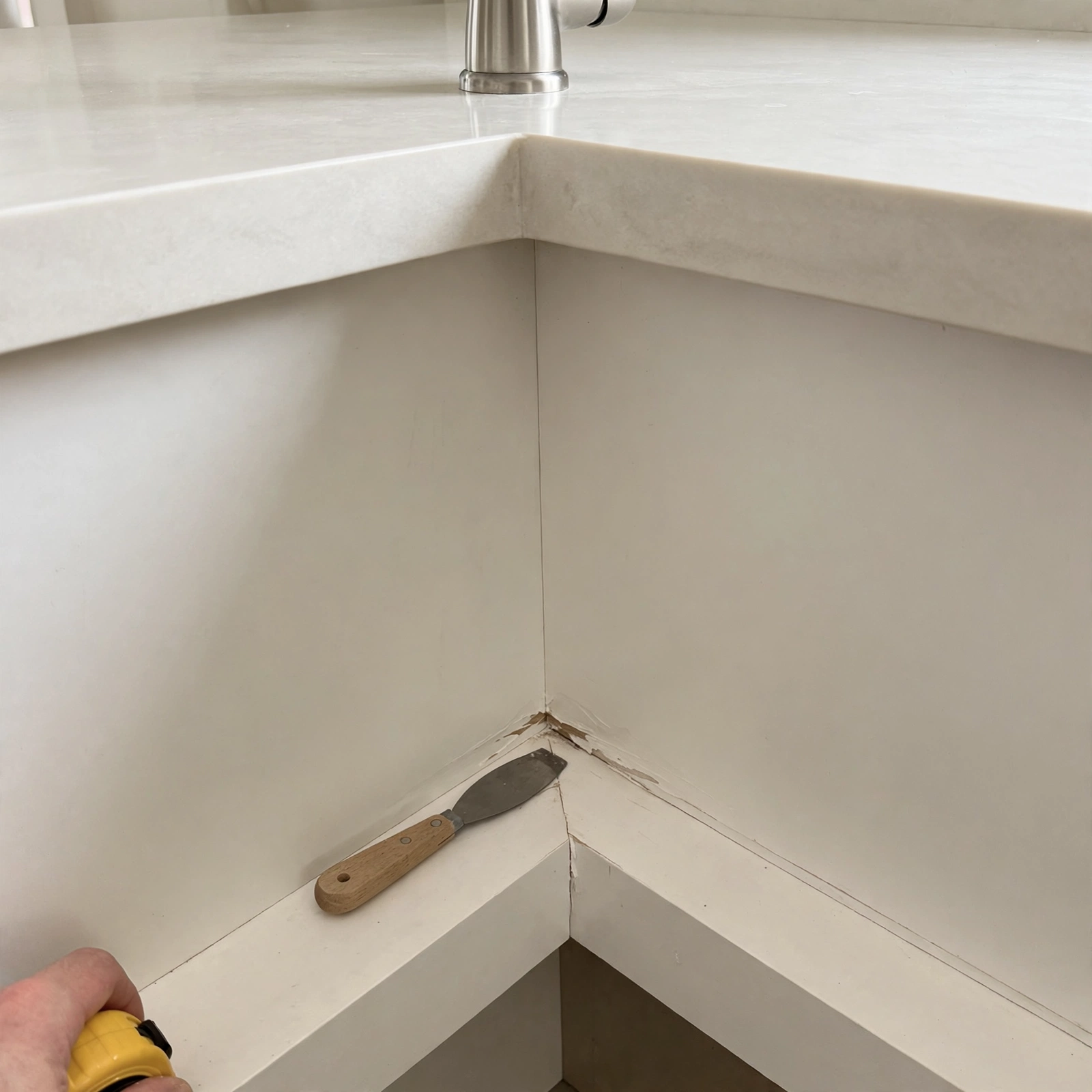 Kitchen counter corner with a faucet and a small scuff on the cabinet baseboard